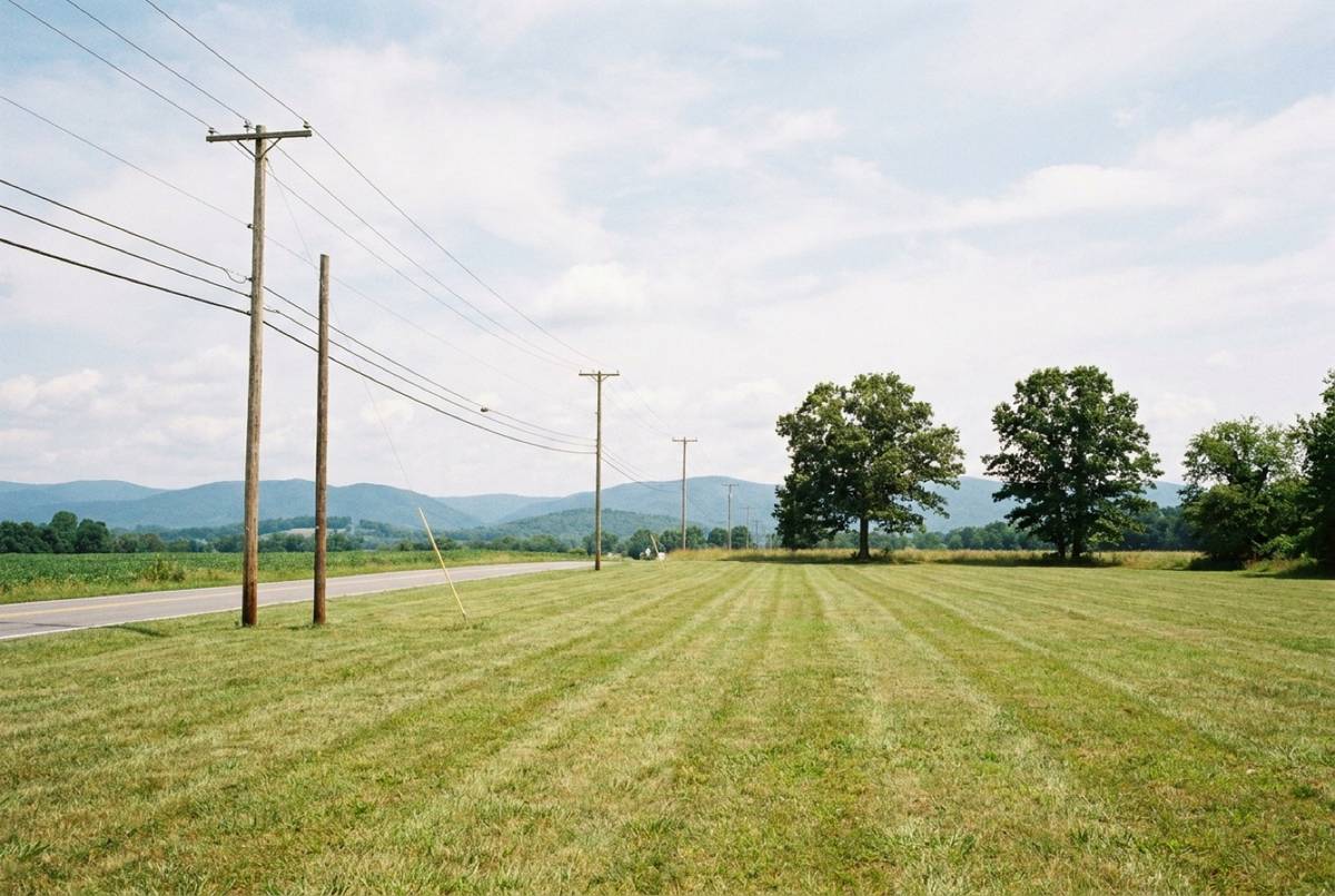 Mowed field along a paved two-lane road with utility poles and power lines, mountains in the distance.